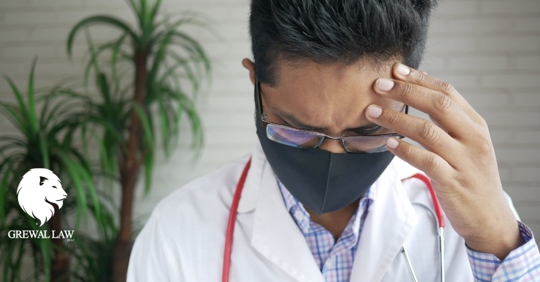 Stressed doctor wearing mask with hand on his forehead.