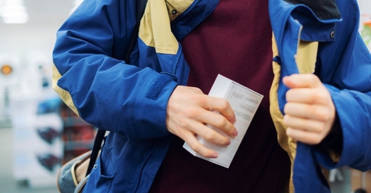 Image of man in a store, hiding a product in a box under his jacket.