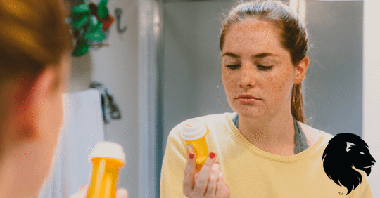 Young woman in front of bathroom mirror holidng a prescription pill bottle