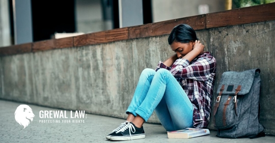 African American college student sitting on pavement with a book and knapsack.
