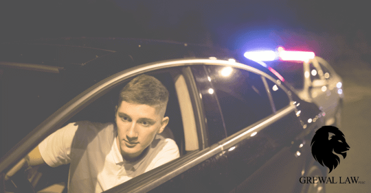 Young man in car looking in rear view mirror with police car behind him.
