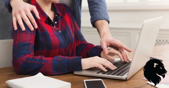 image of a man's hands on a woman's shoulder and his hand over her hand on a laptop keyboard.