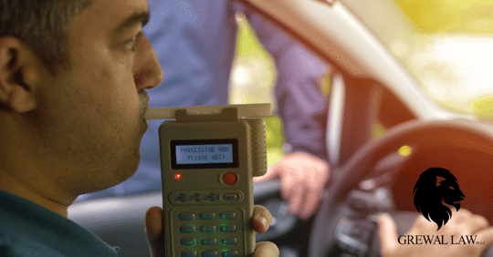 Man in car blowing into a breathalyzer with police officer standing at his window