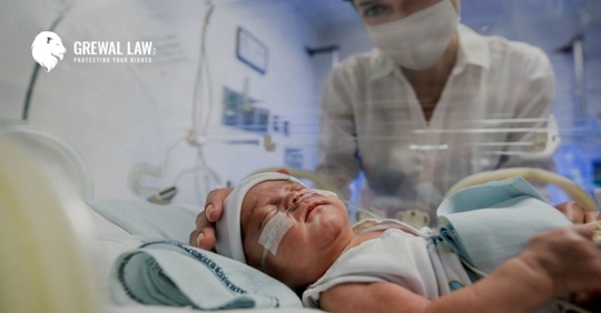 Baby in hospital bassinet with a nurse holding its head.