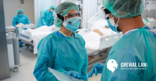 Two doctors in a hospital room talking to each other wearing masks, hair net, goggles and scrubs.