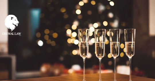 Grewal Law: Four full champagne flutes sitting on a table in front of a lit up Christmas tree.