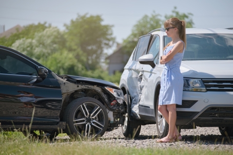 Woman driver standing on street side after car accident.